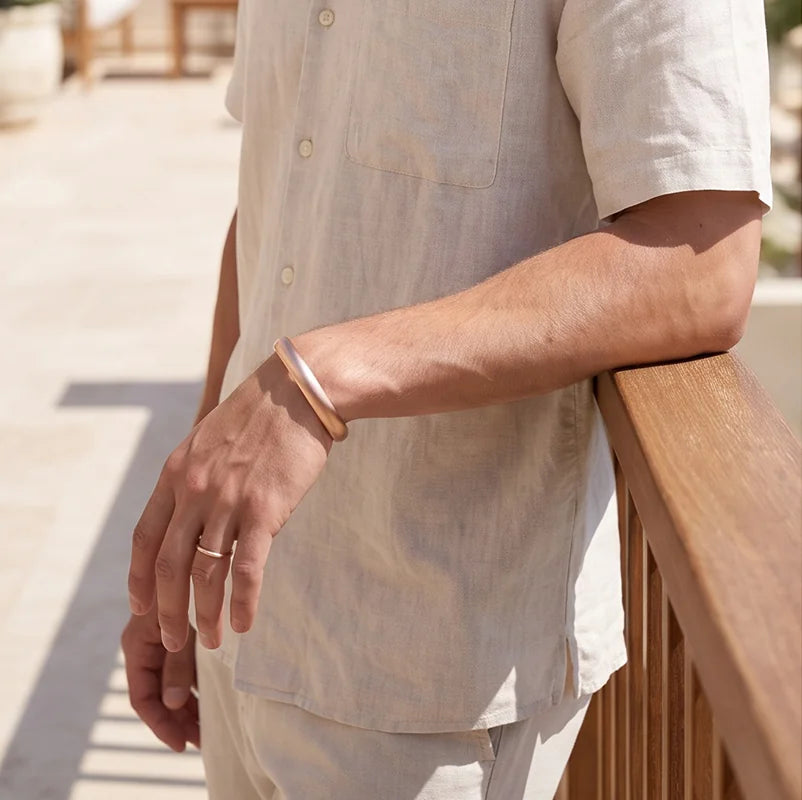 Man wearing solid copper cuff bracelet and matching ring resting arm on outdoor wooden balcony railing