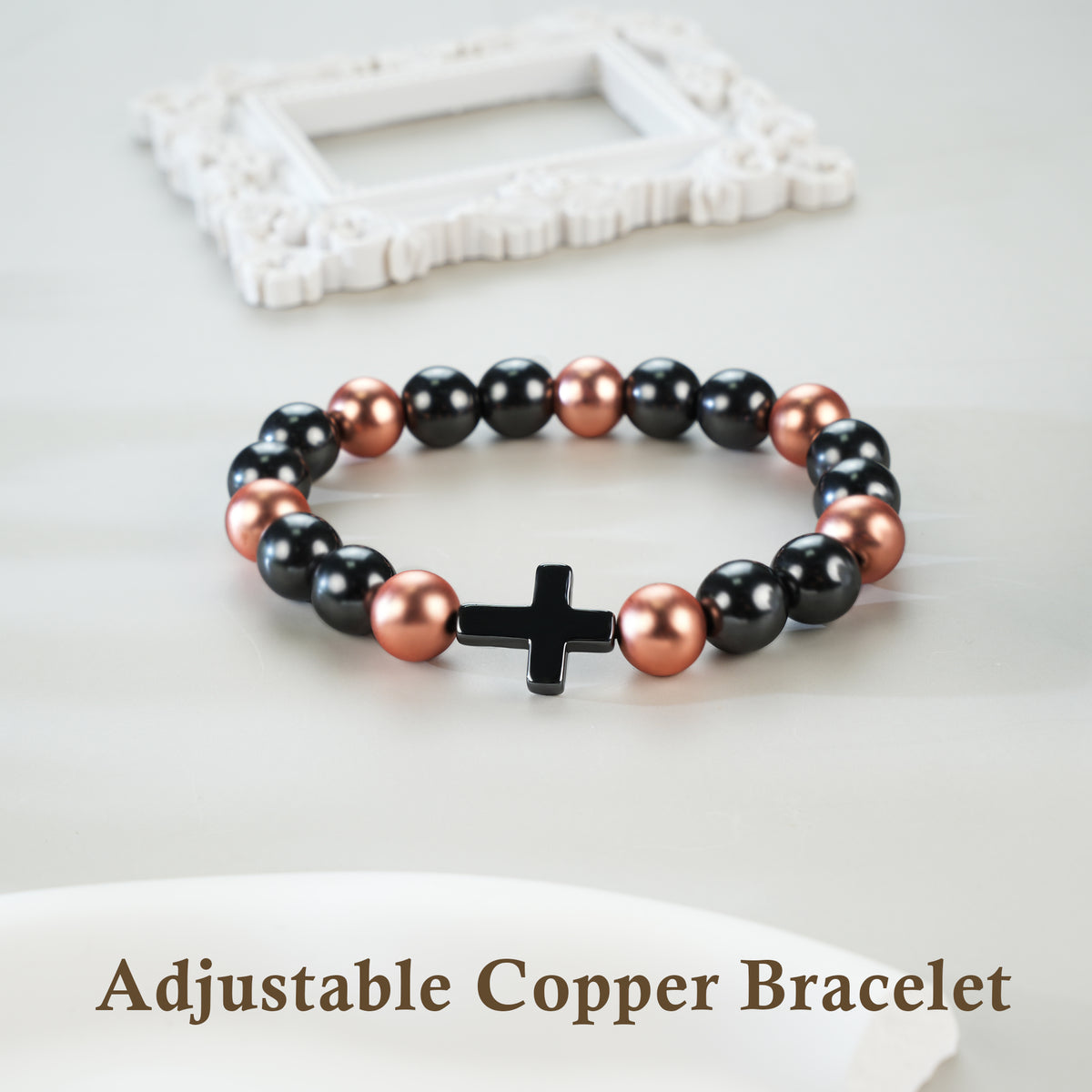Adjustable magnetic copper beaded bracelet with black cross on white tabletop

