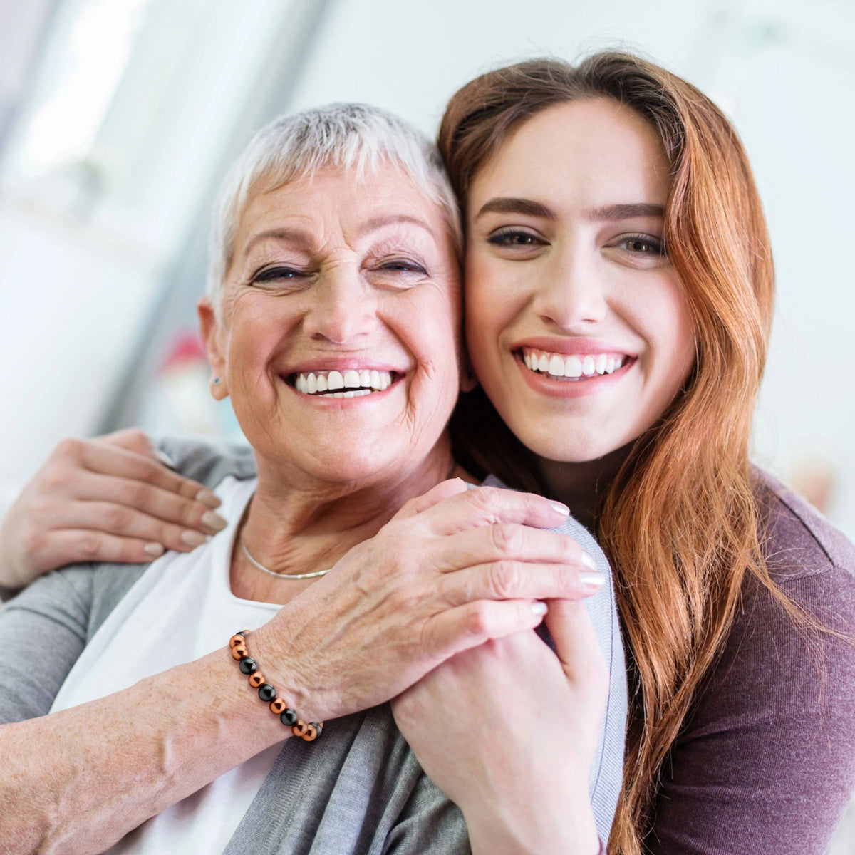 Smiling mother and daughter hugging while mother wears magnetic copper bead bracelet