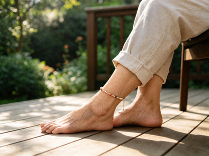 Copper bead anklet with seven colored chakra beads worn on the ankle with cuffed beige linen trousers, adjustable fit, on a wooden garden deck
