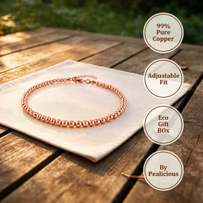 Copper bead anklet on white linen cloth with circular labels reading Copper & Steel Core, Adjustable Fit, Eco Gift Box and By Pealicious