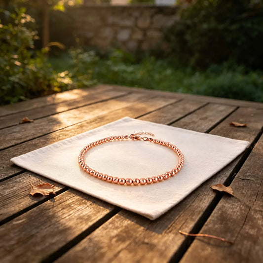 Copper bead anklet for women — 4mm copper beads with steel links and an adjustable extension chain, resting on white linen cloth in a sunlit garden