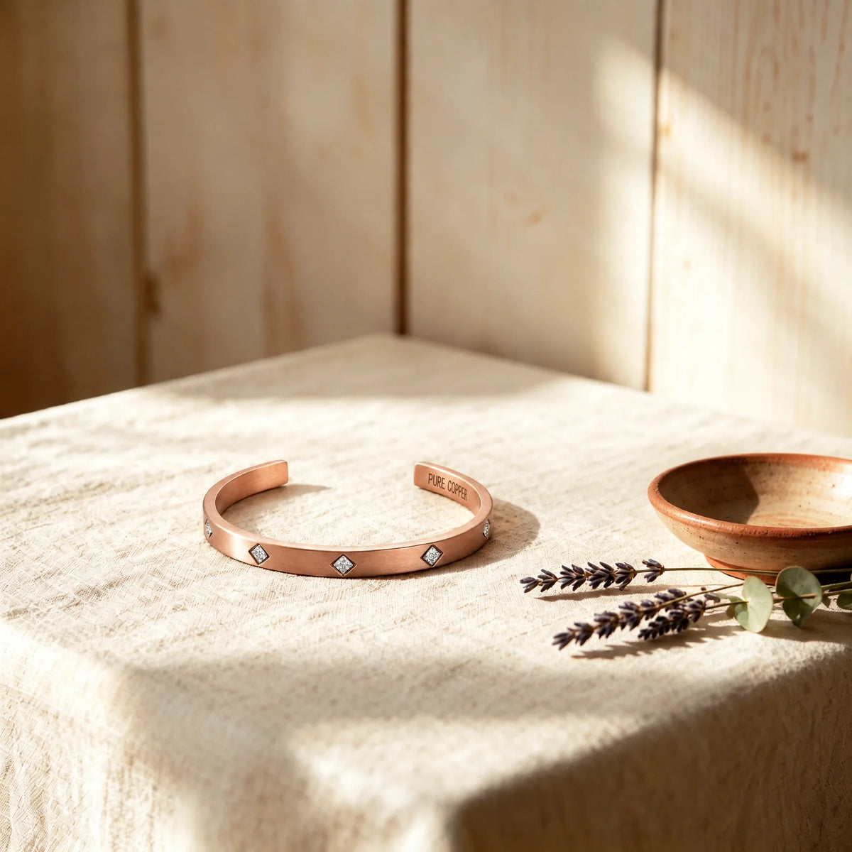 Solid copper Cuff bracelet with bezel-set sparkly cubic zirconia crystals on textured linen display