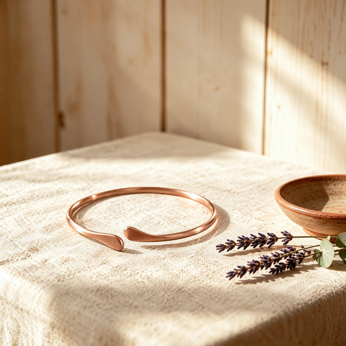 Solid pure copper teardrop open cuff bracelet resting on linen cloth in sunlight