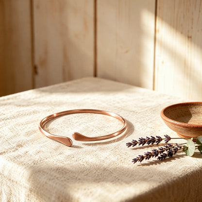Solid pure copper teardrop open cuff bracelet resting on linen cloth in sunlight