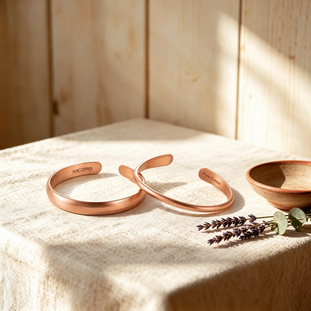 Two pure copper cuffs stamped with Pure Copper on linen table with soft sunlight and lavender
