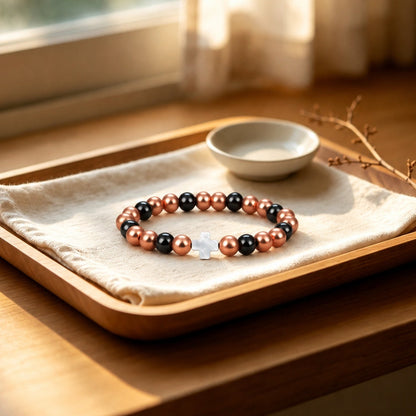 Magnetic copper bead bracelet with white mother-of-pearl cross on wooden tray by window

