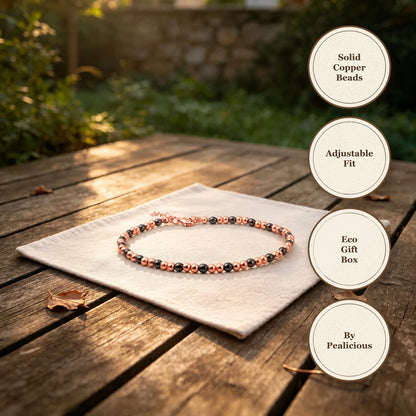 Copper beaded anklet with black magnetic beads and an adjustable chain, resting on white linen over a weathered wooden garden table