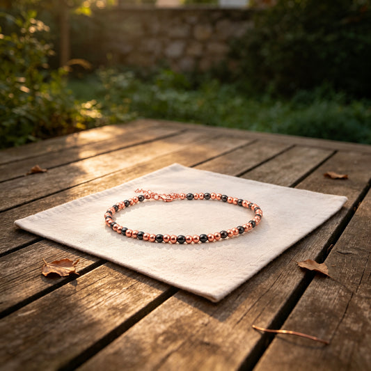 Magnetic copper beaded anklet with black hematite beads on linen cloth over wooden garden table