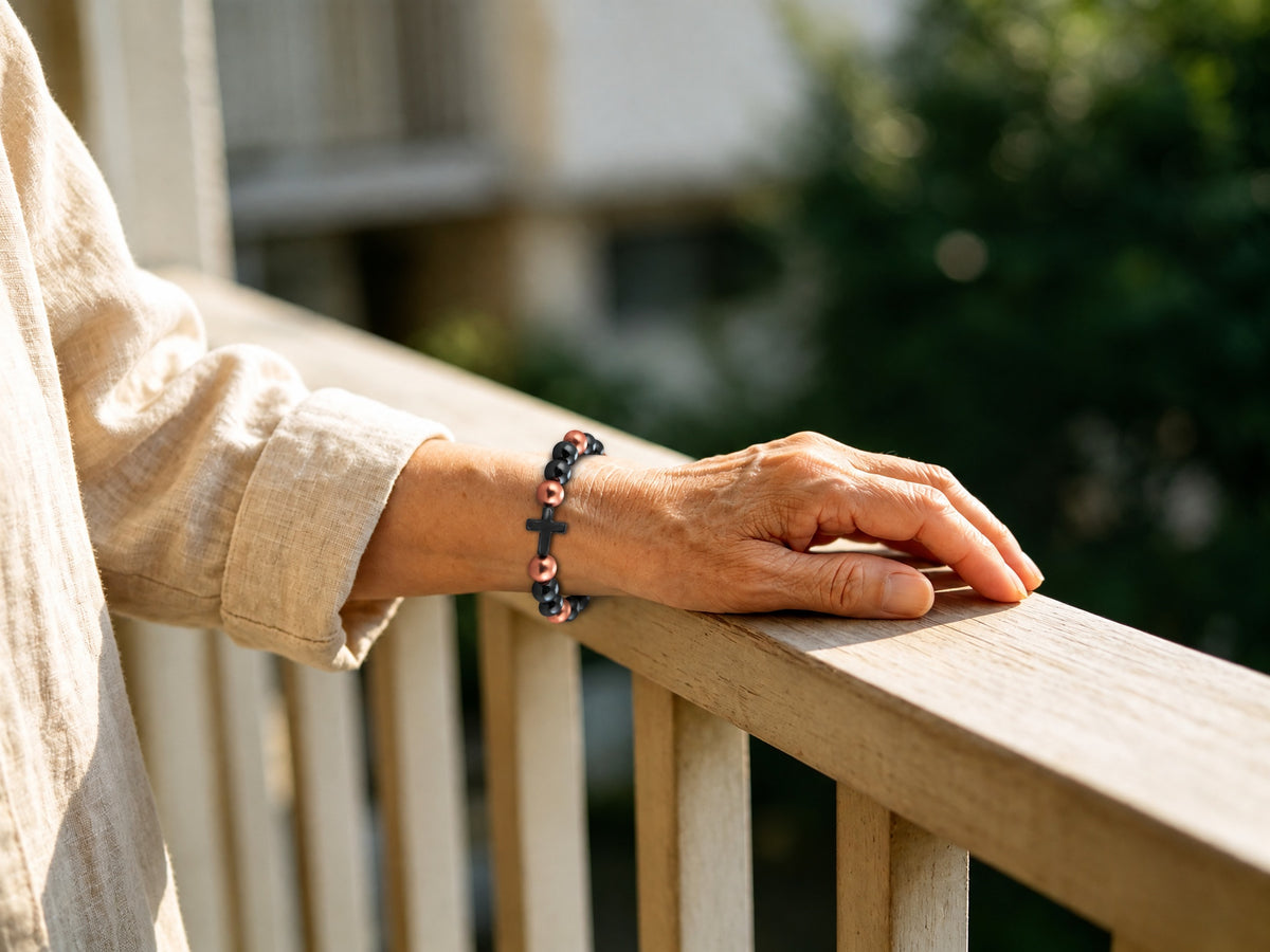  Magnetic copper bead bracelet with black cross worn on wrist outdoors on wooden railing

