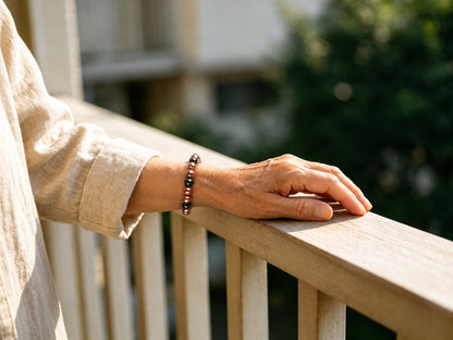 Women's magnetic copper bead bracelet worn on wrist resting on outdoor wooden balcony railing