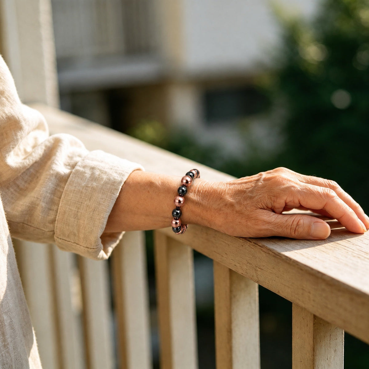 Women's magnetic copper bead bracelet with center accent bead worn on wrist outdoors on wooden railing
