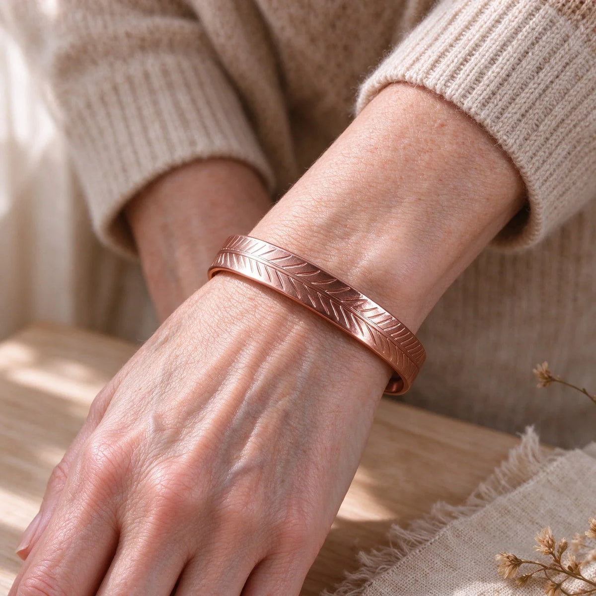   Woman wearing adjustable pure copper feather engraved open cuff bracelet on wrist with knit sweater.
  